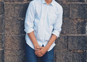 Stylish young man with eyeglasses posing against a brick wall outdoors.