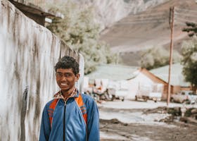 A young man in casual wear smiling in a scenic mountain setting during daylight.